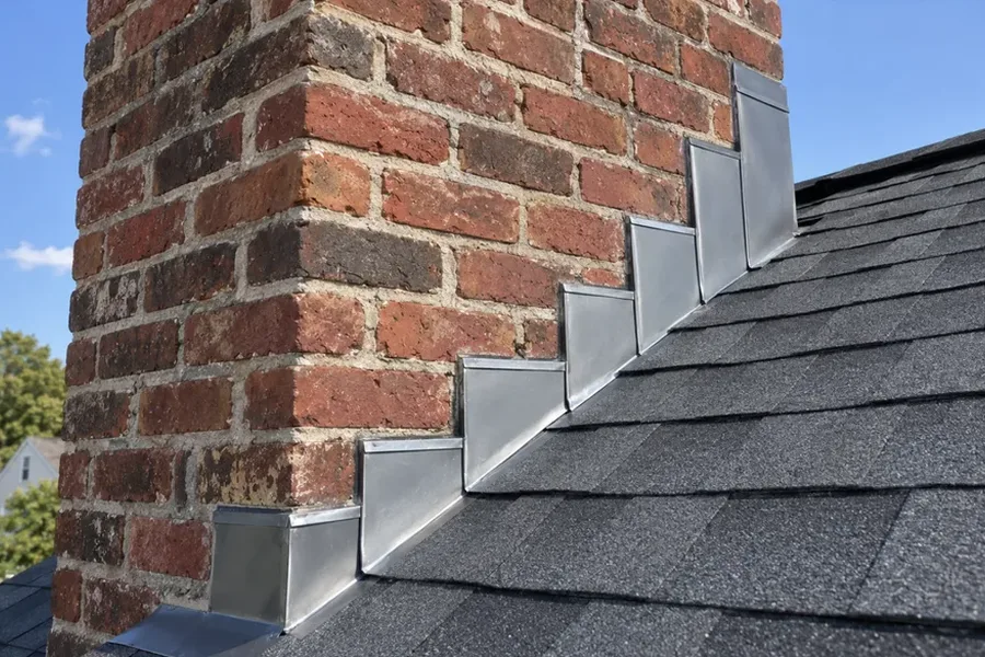 Metal step flashing where asphalt shingles meet a brick chimney